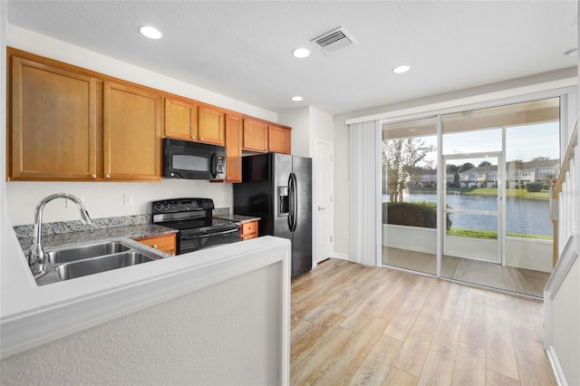 kitchen featuring sink, black appliances, a water view, and light hardwood / wood-style flooring