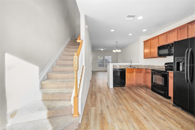 kitchen featuring pendant lighting, black appliances, sink, a notable chandelier, and light hardwood / wood-style flooring