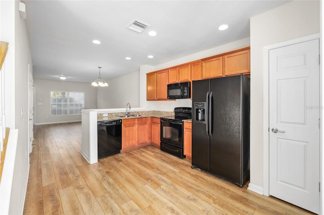 kitchen with pendant lighting, black appliances, kitchen peninsula, sink, and light hardwood / wood-style flooring