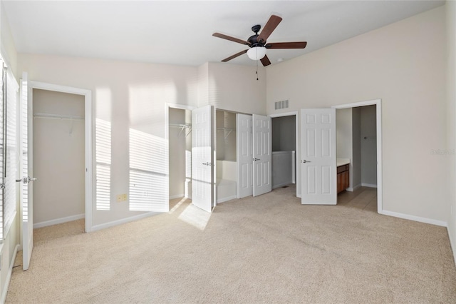 unfurnished bedroom with ceiling fan, two closets, and light colored carpet