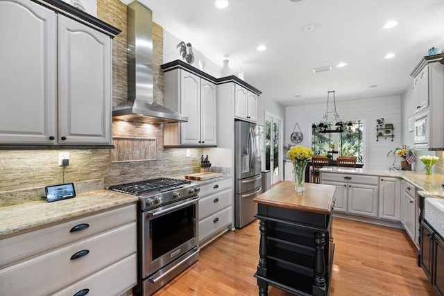 kitchen featuring wooden counters, wall chimney range hood, light hardwood / wood-style flooring, decorative backsplash, and appliances with stainless steel finishes