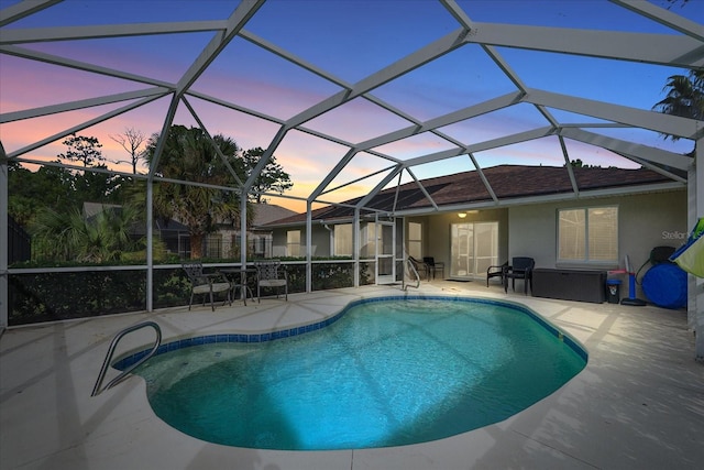 pool at dusk featuring glass enclosure and a patio