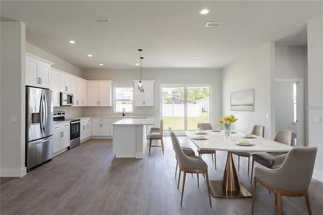 kitchen with hardwood / wood-style floors, decorative light fixtures, a kitchen island, white cabinetry, and stainless steel appliances