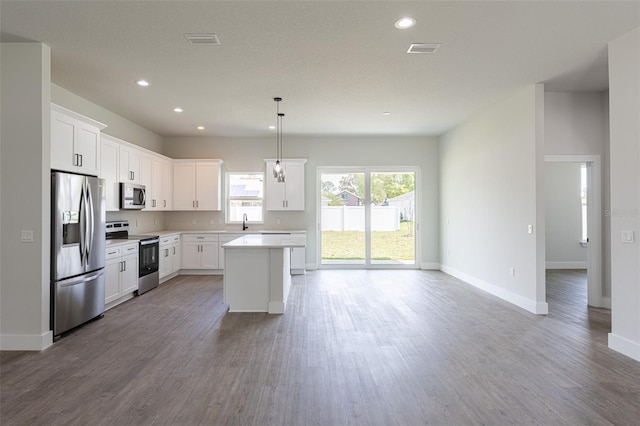 kitchen featuring white cabinets, hanging light fixtures, hardwood / wood-style flooring, appliances with stainless steel finishes, and a kitchen island