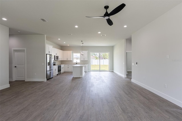 kitchen featuring appliances with stainless steel finishes, hardwood / wood-style flooring, white cabinets, a center island, and hanging light fixtures