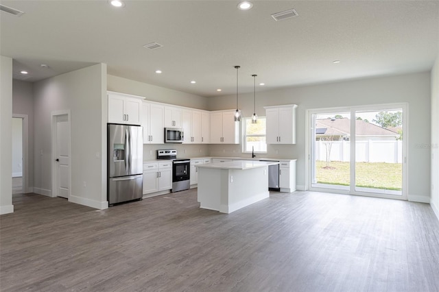 kitchen featuring pendant lighting, white cabinets, a kitchen island, wood-type flooring, and stainless steel appliances