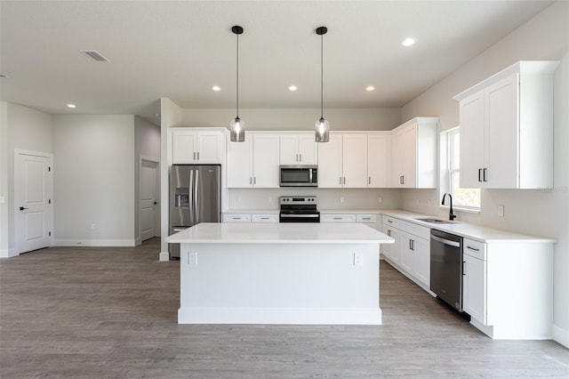 kitchen with a center island, white cabinets, sink, decorative light fixtures, and stainless steel appliances