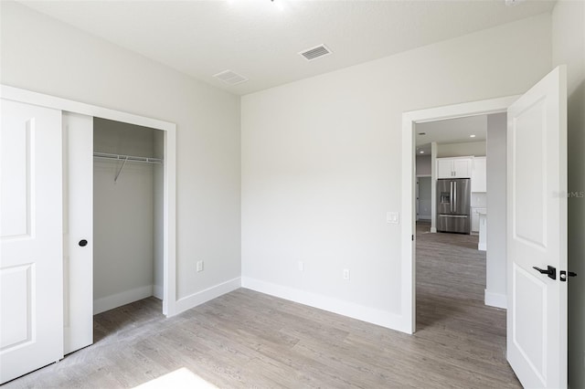 unfurnished bedroom with stainless steel fridge with ice dispenser, light hardwood / wood-style flooring, and a closet