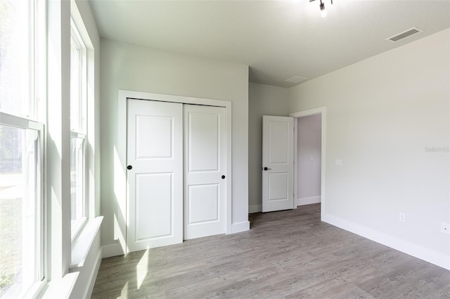 unfurnished bedroom with a textured ceiling, a closet, light hardwood / wood-style floors, and multiple windows