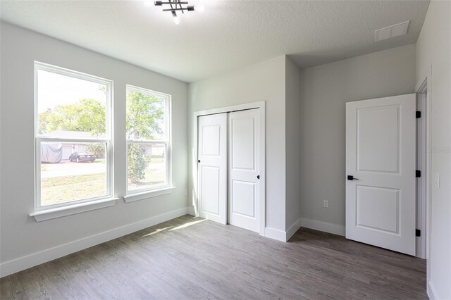 unfurnished bedroom featuring a textured ceiling, dark hardwood / wood-style flooring, and a closet