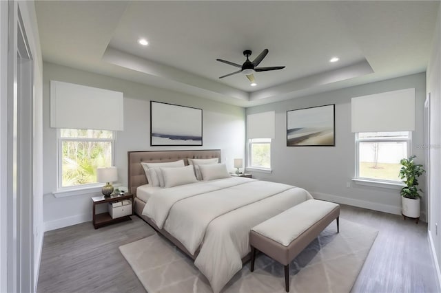 bedroom with ceiling fan, a raised ceiling, and multiple windows