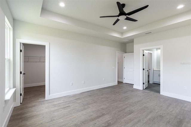 unfurnished bedroom featuring ensuite bath, a spacious closet, ceiling fan, hardwood / wood-style floors, and a closet