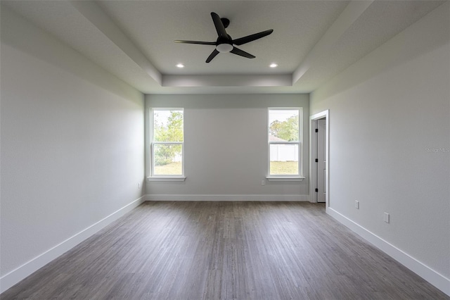 empty room with a raised ceiling, ceiling fan, a healthy amount of sunlight, and dark hardwood / wood-style floors