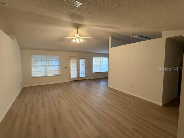 unfurnished living room with hardwood / wood-style floors, french doors, vaulted ceiling, ceiling fan, and a textured ceiling