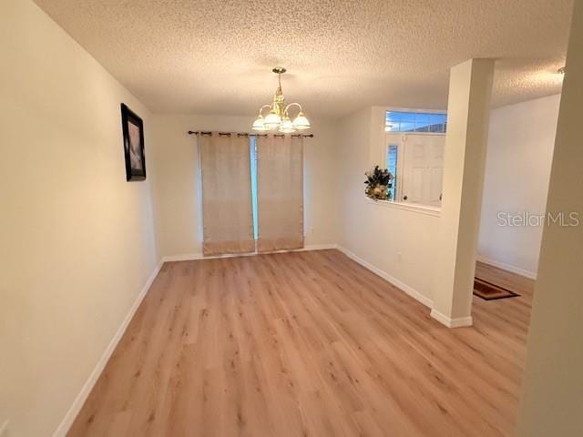 empty room featuring a notable chandelier, a textured ceiling, and light hardwood / wood-style flooring