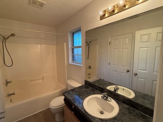 full bathroom with wood-type flooring, a textured ceiling, toilet, vanity, and shower / bathtub combination