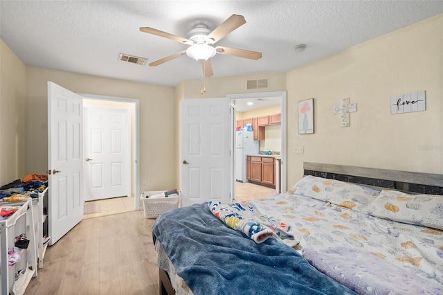 bedroom featuring ceiling fan, white fridge, light hardwood / wood-style floors, and a textured ceiling