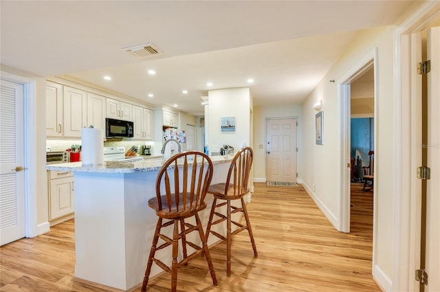 kitchen featuring a kitchen breakfast bar, light stone counters, light hardwood / wood-style flooring, and a kitchen island