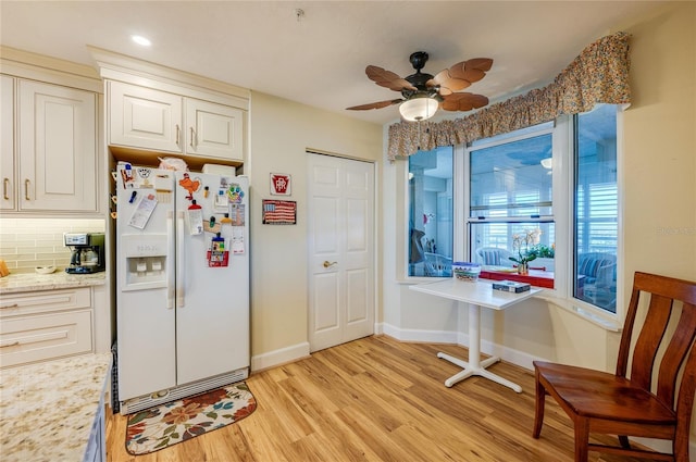 kitchen with light stone countertops, backsplash, ceiling fan, light hardwood / wood-style floors, and white fridge with ice dispenser