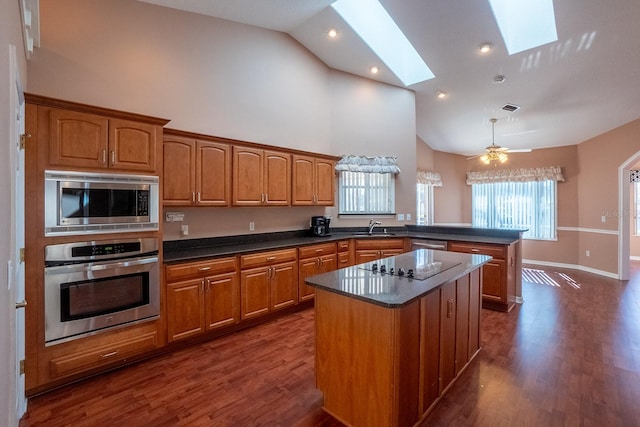 kitchen with a skylight, stainless steel appliances, ceiling fan, a center island, and dark hardwood / wood-style floors