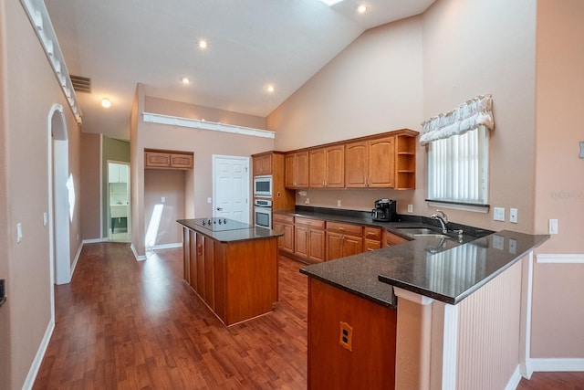 kitchen featuring kitchen peninsula, sink, appliances with stainless steel finishes, a kitchen island, and wood-type flooring