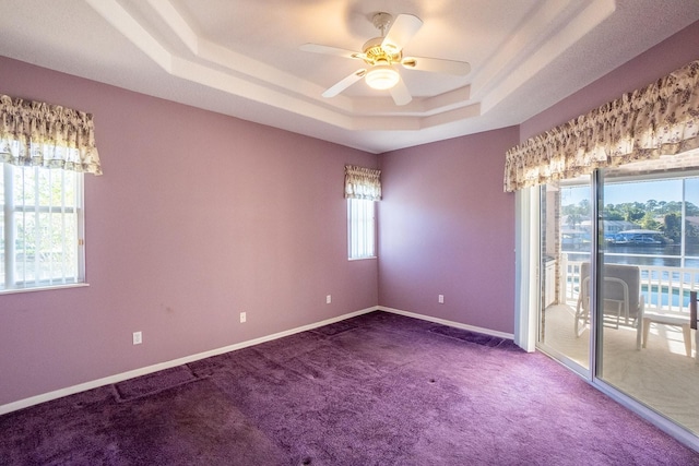 carpeted spare room with a water view, a wealth of natural light, a tray ceiling, and ceiling fan