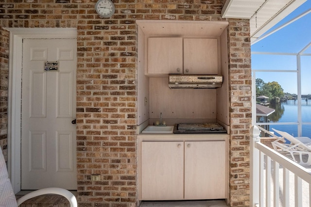 kitchen featuring sink, brick wall, ventilation hood, light brown cabinetry, and a water view