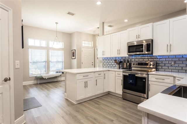 kitchen featuring kitchen peninsula, appliances with stainless steel finishes, pendant lighting, light hardwood / wood-style floors, and white cabinetry