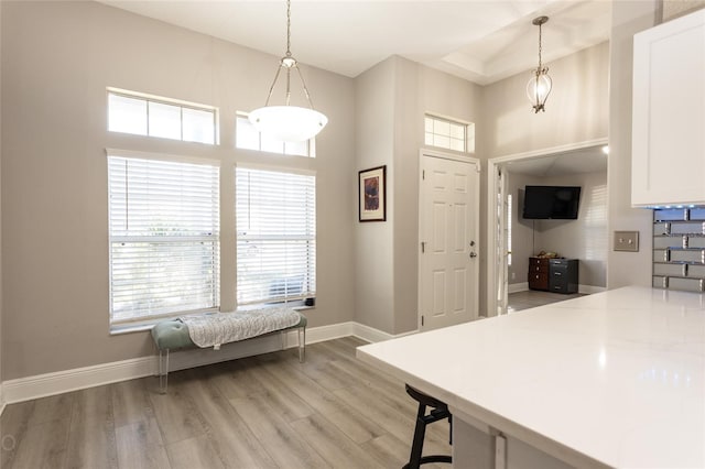 kitchen featuring a towering ceiling, light hardwood / wood-style floors, white cabinetry, and hanging light fixtures