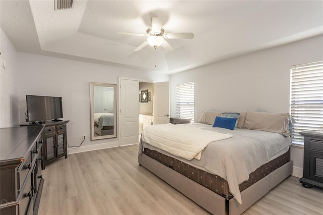 bedroom with a tray ceiling, connected bathroom, ceiling fan, and light hardwood / wood-style floors