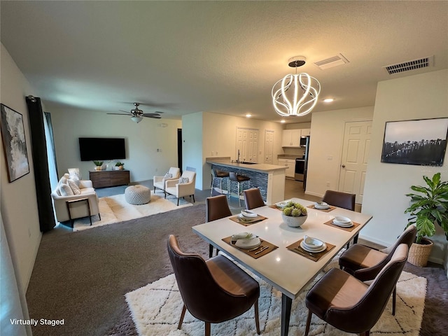 dining space featuring a textured ceiling, ceiling fan with notable chandelier, light colored carpet, and sink