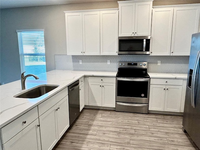 kitchen with light wood-type flooring, light stone counters, stainless steel appliances, sink, and white cabinetry