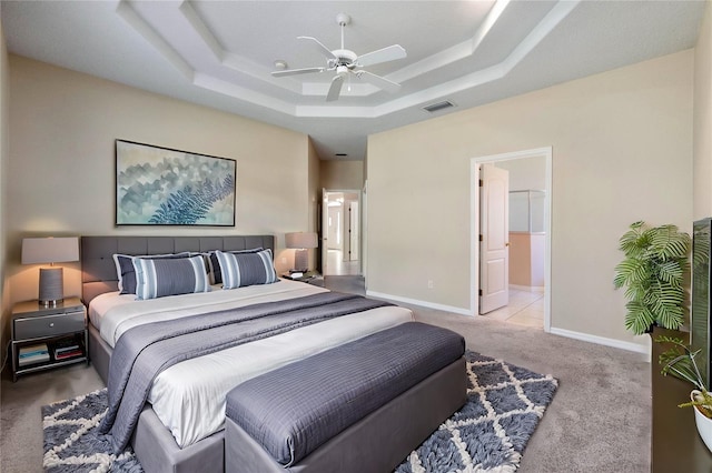 bedroom featuring connected bathroom, light colored carpet, ceiling fan, and a tray ceiling