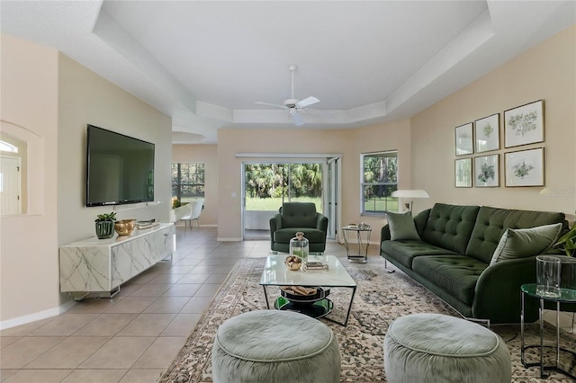 living room with a tray ceiling, ceiling fan, and light tile patterned floors