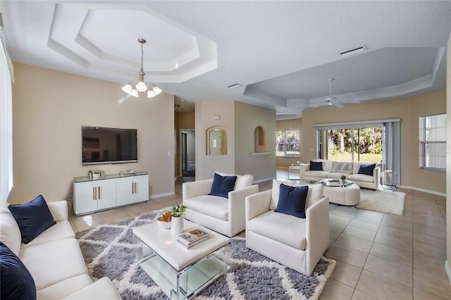 living room with a raised ceiling, a textured ceiling, light tile patterned floors, and ceiling fan with notable chandelier