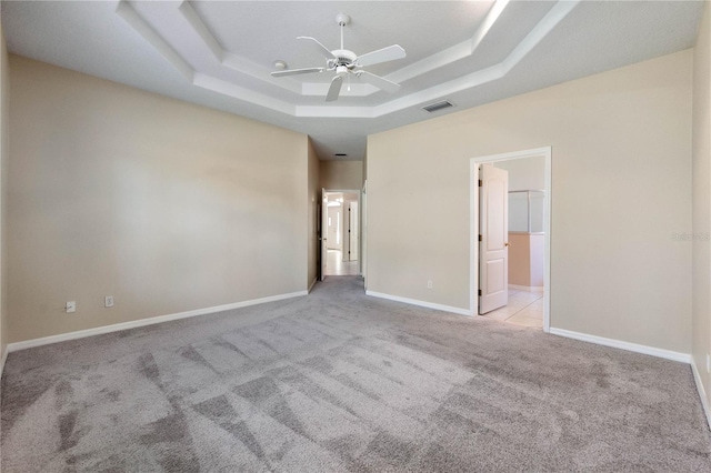 empty room featuring a tray ceiling, ceiling fan, and light colored carpet