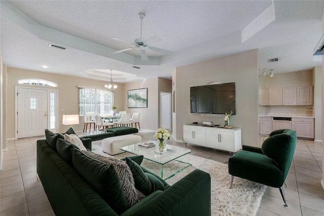 living room featuring a tray ceiling, ceiling fan with notable chandelier, light tile patterned floors, and a textured ceiling