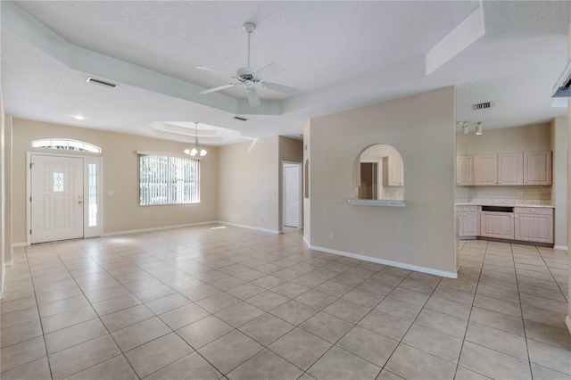 unfurnished living room with a textured ceiling, ceiling fan with notable chandelier, a tray ceiling, and light tile patterned flooring