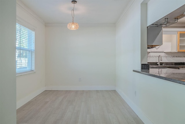 unfurnished dining area with crown molding, baseboards, light wood finished floors, and a sink