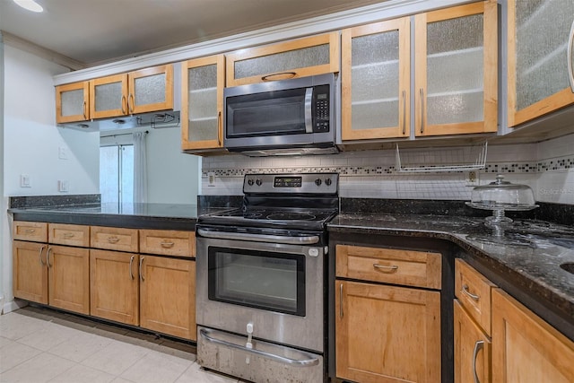 kitchen with decorative backsplash, dark stone countertops, stainless steel appliances, crown molding, and glass insert cabinets