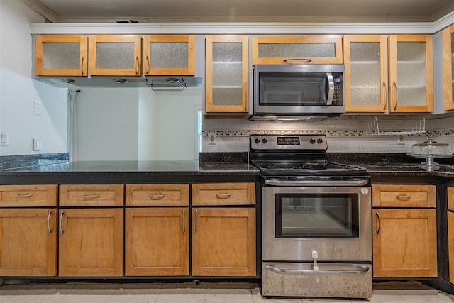 kitchen with dark stone countertops, stainless steel appliances, decorative backsplash, glass insert cabinets, and brown cabinets