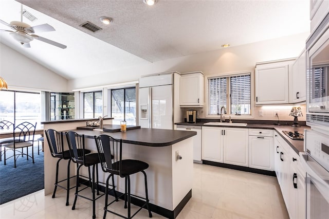 kitchen with ceiling fan, a center island, white cabinetry, a kitchen bar, and dishwashing machine