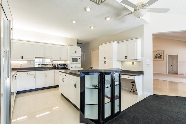 kitchen with decorative backsplash, white appliances, light tile patterned floors, white cabinets, and a center island