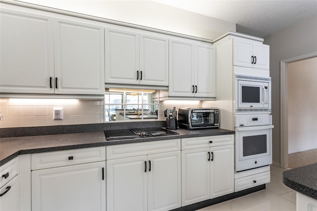 kitchen with backsplash, white appliances, a textured ceiling, light tile patterned floors, and white cabinets