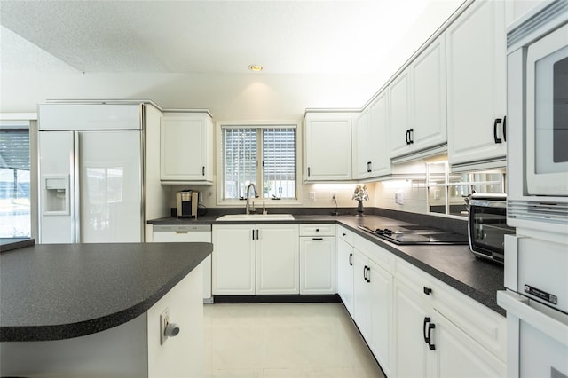 kitchen featuring sink, light tile patterned floors, built in appliances, decorative backsplash, and white cabinets