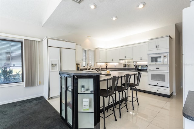 kitchen featuring white cabinets, a center island with sink, built in appliances, light tile patterned floors, and a kitchen bar