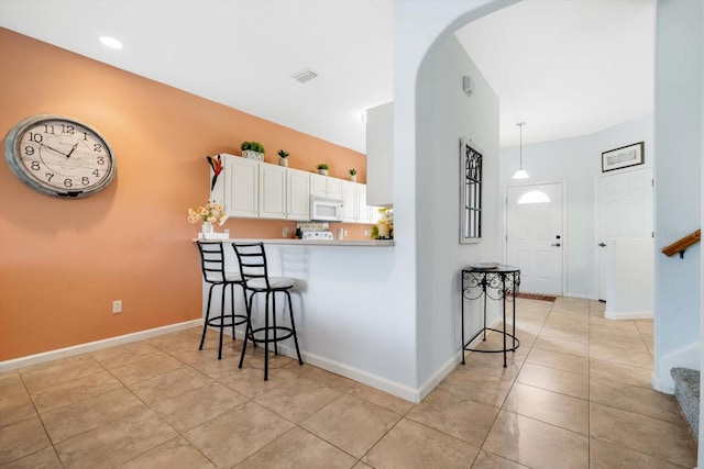 kitchen featuring white cabinetry, decorative light fixtures, light tile patterned flooring, kitchen peninsula, and a breakfast bar area