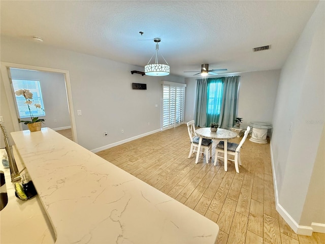 dining area with ceiling fan, light hardwood / wood-style flooring, and a textured ceiling