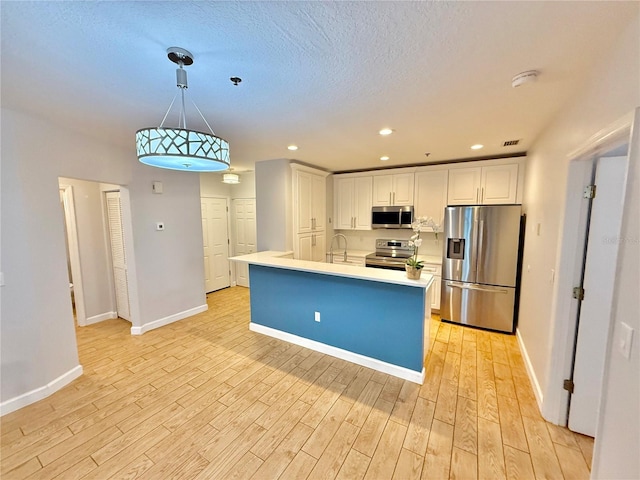 kitchen with white cabinets, hanging light fixtures, appliances with stainless steel finishes, and light hardwood / wood-style flooring