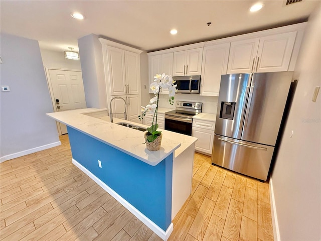 kitchen featuring stainless steel appliances, white cabinetry, light hardwood / wood-style floors, and an island with sink